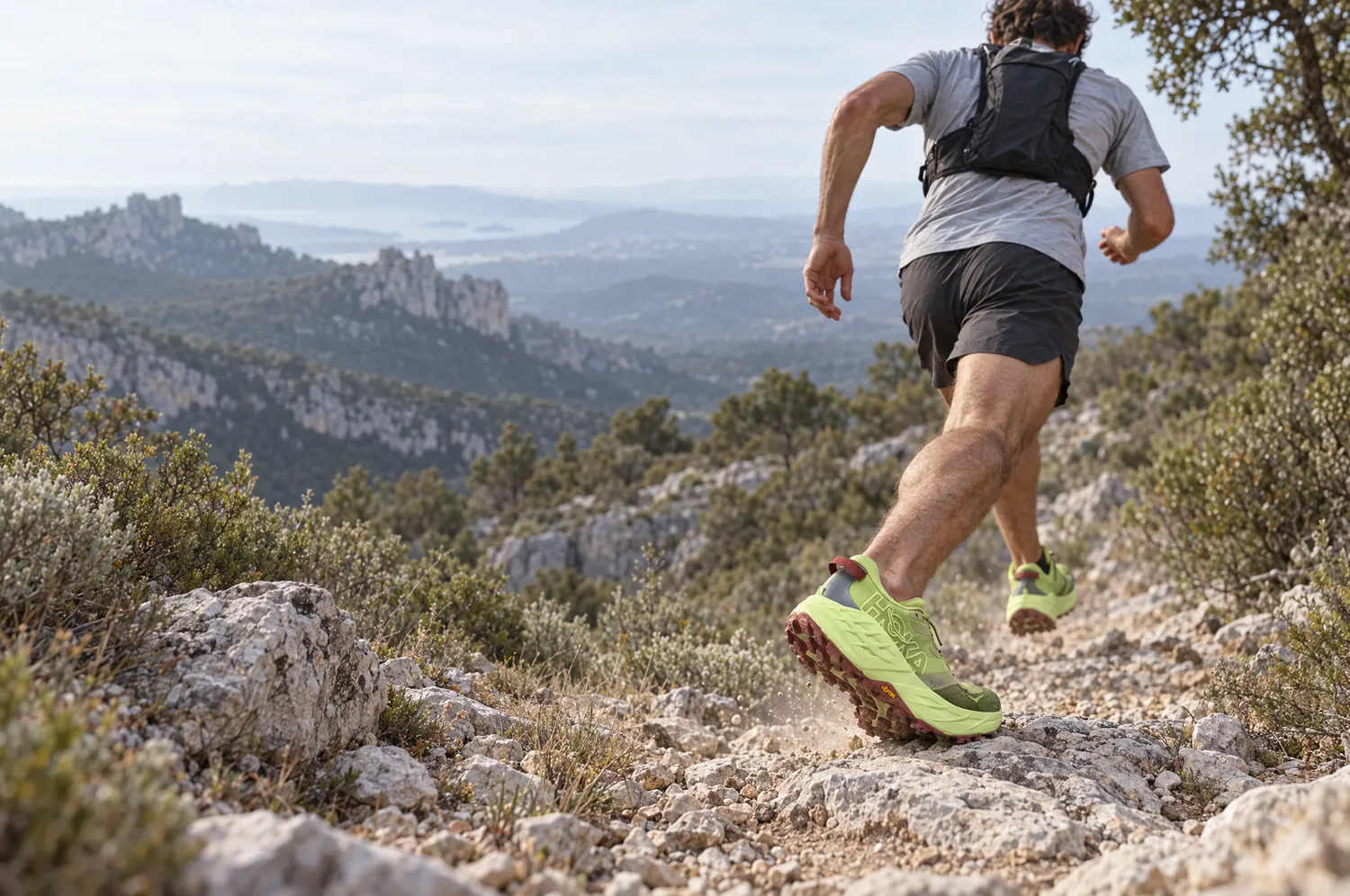 Traileur en pleine descente sur un sentier calcaire de Provence, chaussures de trail au premier plan
