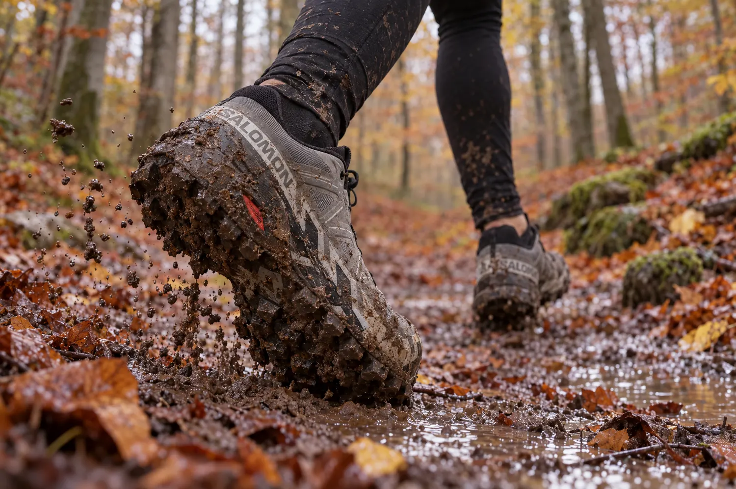 Chaussure de trail aux crampons profonds couverts de boue, sur un sentier forestier en automne